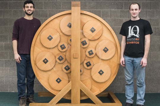 students flanking giant wooden book wheel with sets of interlocking gears.