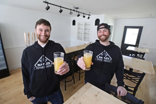 two brewing company owners holding up glasses of beer.