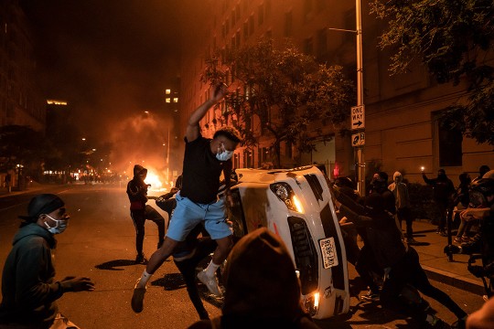 protestors overturning a car in a street at night.