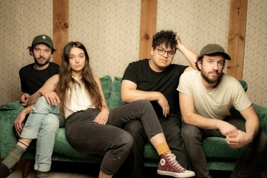 four band members sitting on a couch.