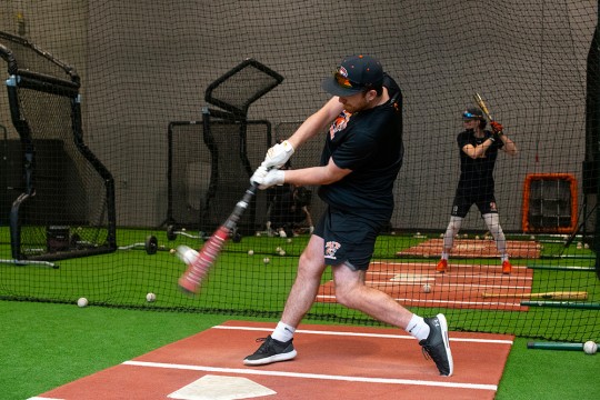 athlete in a batting cage swinging a baseball bat.