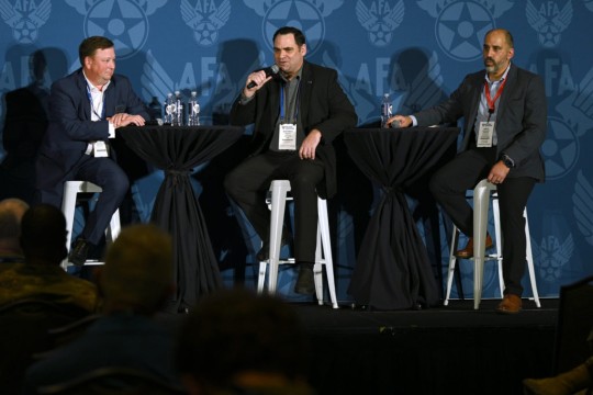 three panelists sitting at high top tables on a stage.