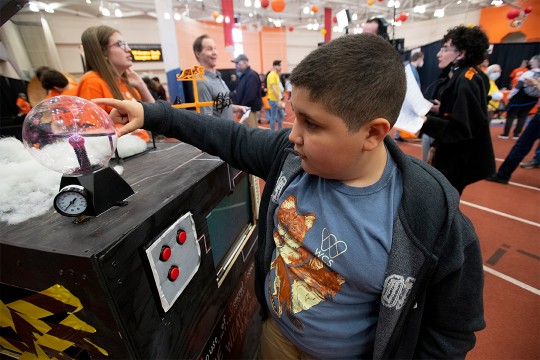Nine-year-old boy touches a glass ball with small purple electrical bolts. 