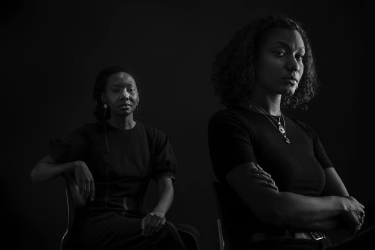 woman sitting in a chair and another woman standing with her arms crossed.