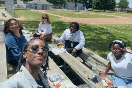 five people sitting on wooden bleachers eating food.