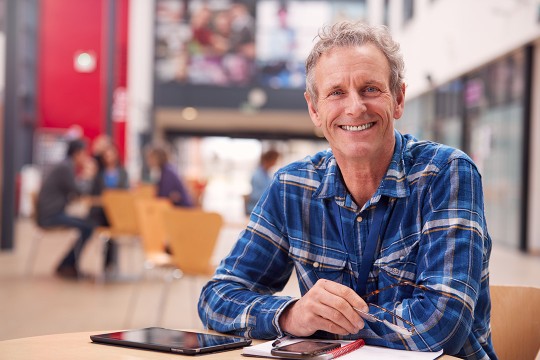 retired man sitting at a table with a tablet and a phone.