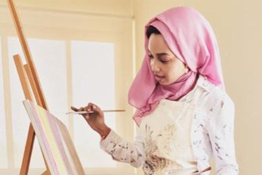 Zulfa Rasheed works on a painting that is leaning against an easel.
