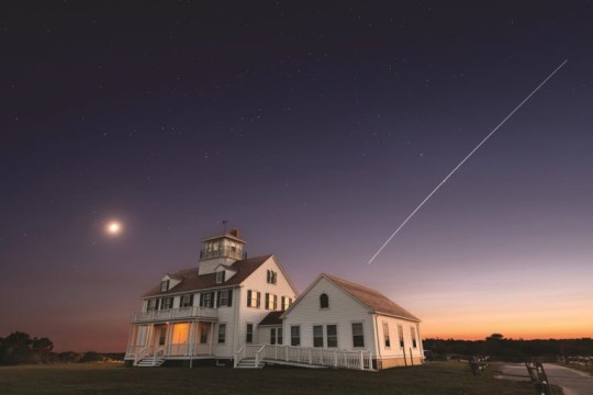 a house with a bright light and steak in the sky in the background.