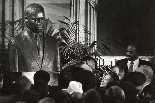 a black and white image of a group of people facing Coretta Scott King as she reacts to an MLK portrait being unveiled