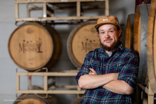 Phil Plummer stands with his arms crossed in front of wine barrels.