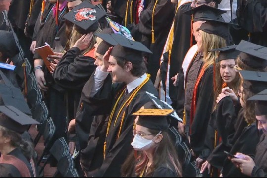 graduates in regalia are shown seated in rows in an auditorium.