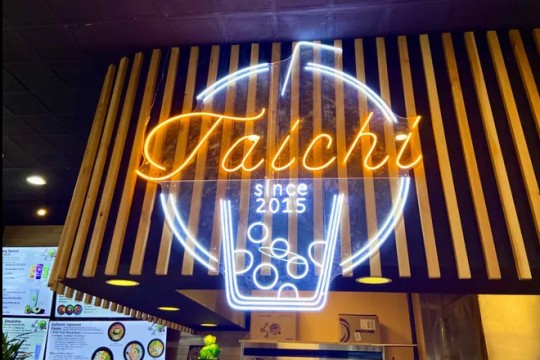 a neon sign that reads Taichi since 2015 glows above a cashier station in a storefront.