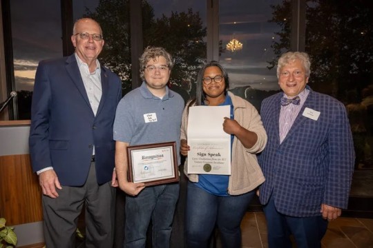 Four people stand for a posed photo with two recognition plaques.