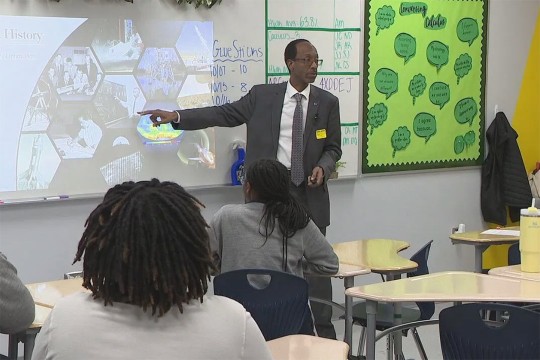 Clayton Turner stands in front of a classroom full of students pointing at a smart screen.