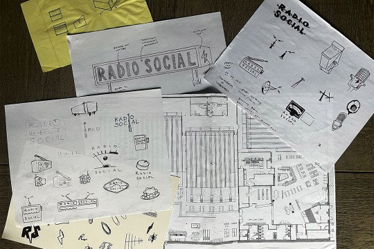 white and yellow paper covered with ideas and designs for the restauraunt Radio Social are strewn across a wooden table.
