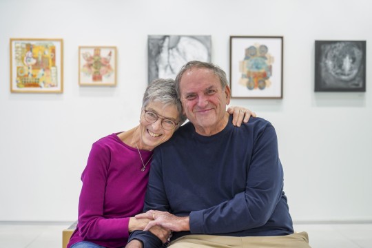 Jean and Bill Stephens hold hands in front of a gallery exhibition of their work.