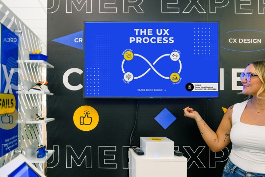 Julia Tenney stands next to a digital display of UI/UX and product designs.