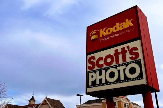 a store sign for Scotts Photo appears under a Kodak sign on the side of the street.