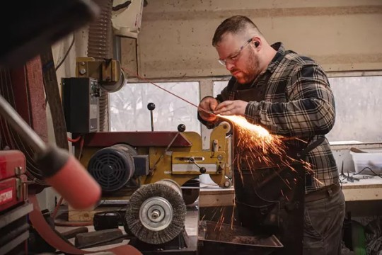 Man grinding metal with sparks flying in a workshop.