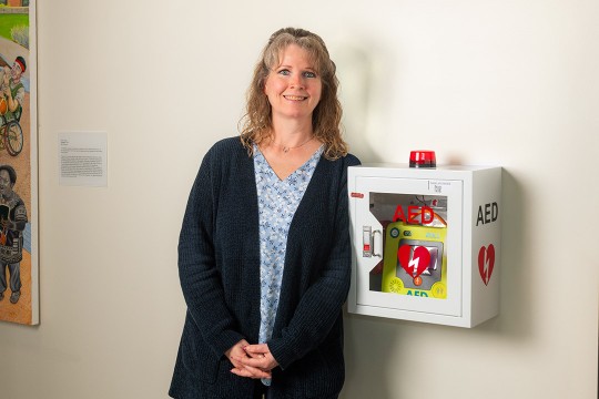 a woman stands next to an A E D device attached to a wall.