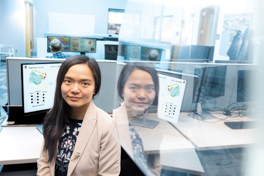 a woman sits in a brightly lit cubicle with a mirror image shown on the right.