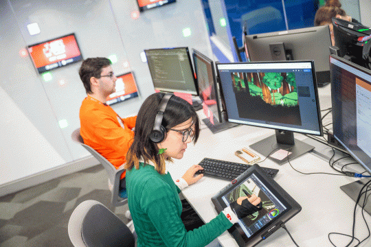 Two students sit in a modern and brightly lit computer lab, working on a video game.