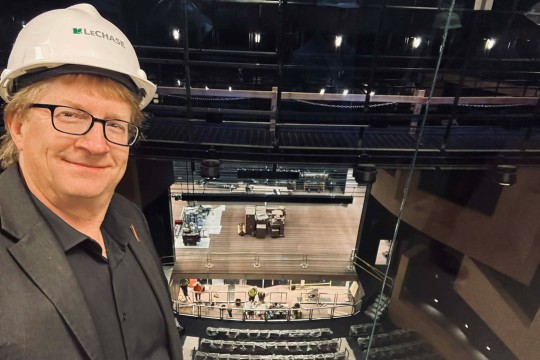 a man stands in the upper area of a performing arts building with a stage in the background.
