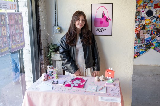 A student stands in front of a table displayed with pink art objects