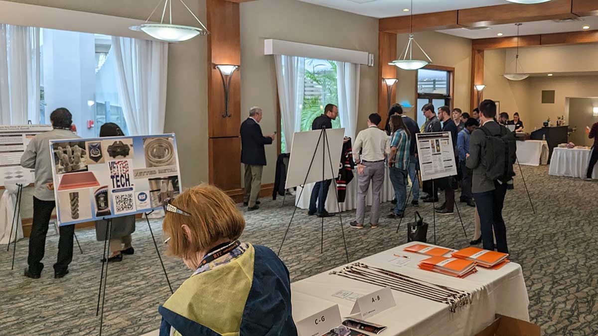 people attending a symposium, listening to poster presentations and visiting display tables.