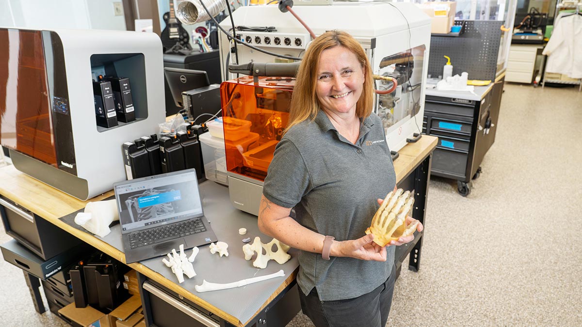 researcher poses in a lab holding a realistic human hand, with the bone structure visible.