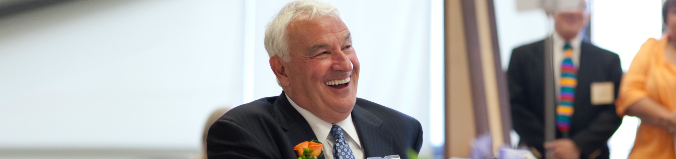 Tom golisano laughing while sitting in a suit