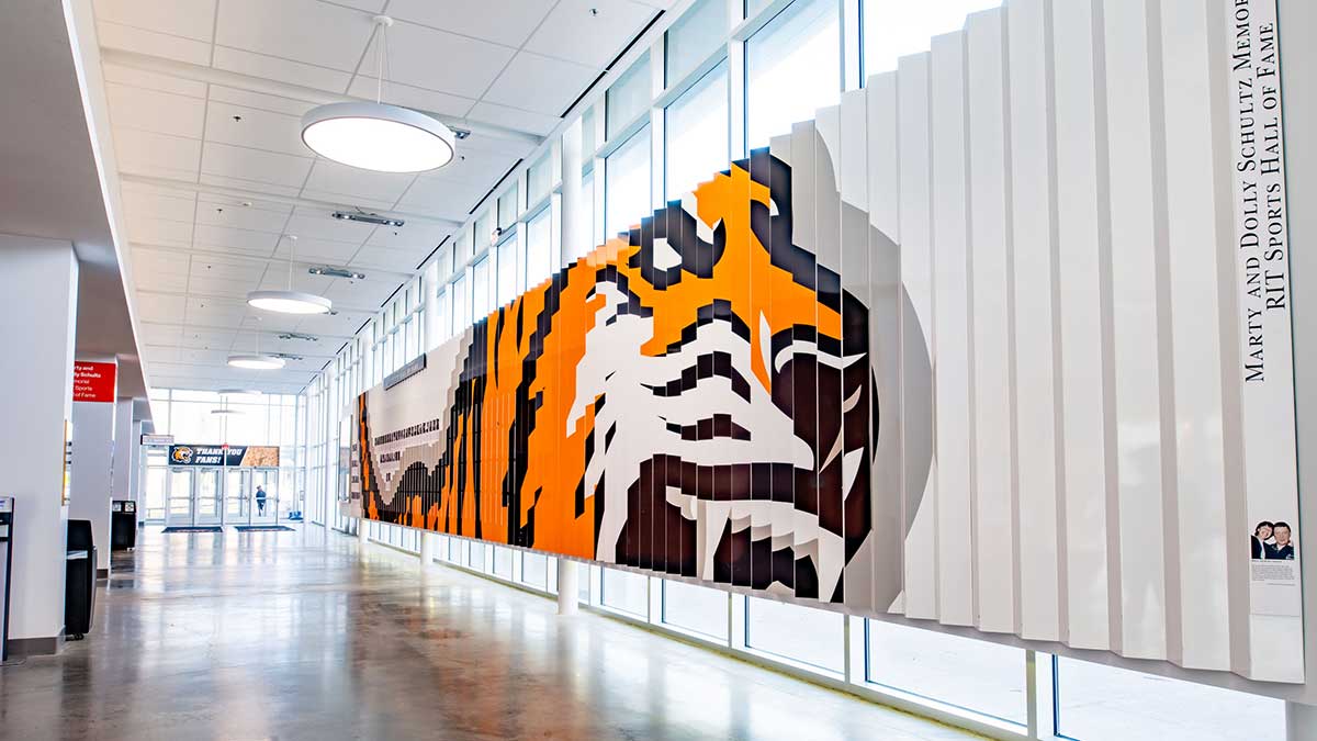 A bright lobby hallway featuring a large vertical tiger mural and the RIT Sports Hall of Fame signage.