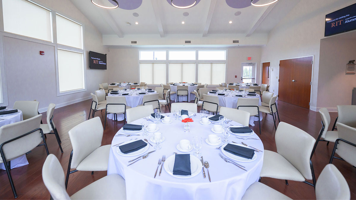 A banquet-style room with round tables set for a formal event with white tablecloths and black napkins.
