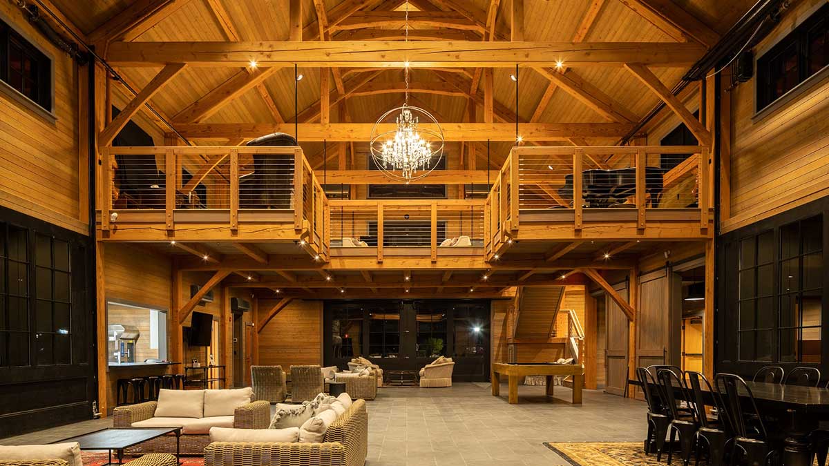 A spacious lodge with timber framing, a central chandelier, loft seating, and cozy furniture for gatherings.