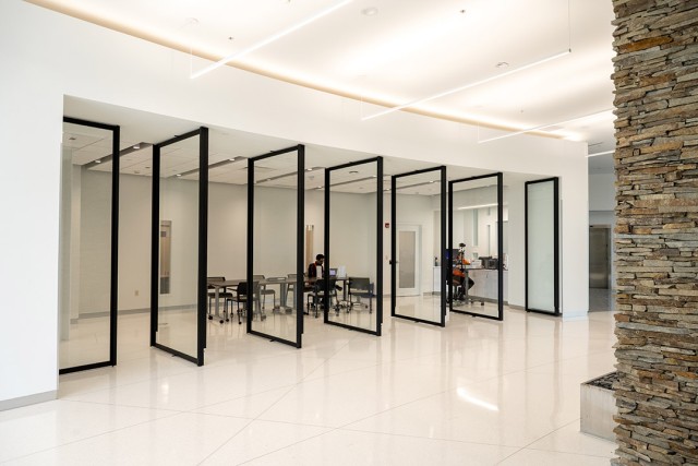 People work at desks behind floor-to-ceiling glass panels in a modern office lobby.