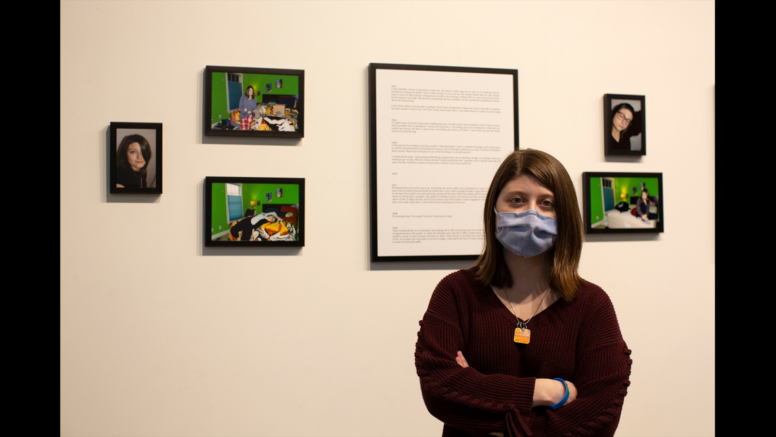 A student poses in front of her photo work on a wall.