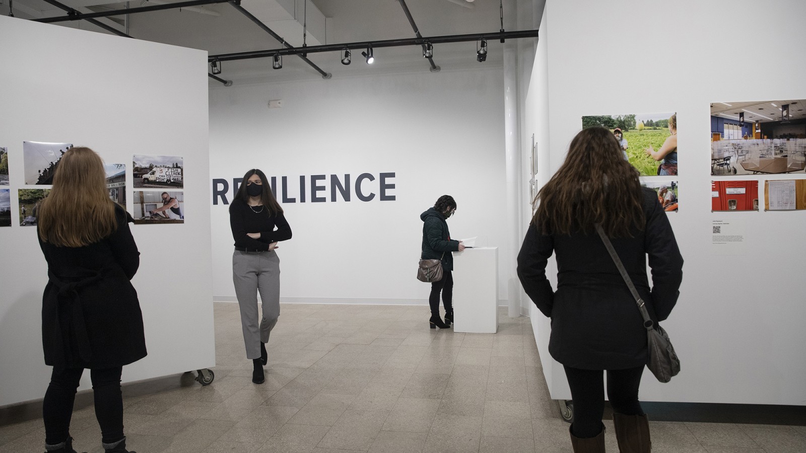 People look at photos on a wall in a gallery.