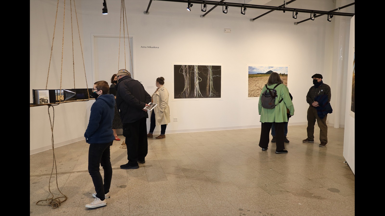 Gallery visitors look at are on the wall and suspended from the ceiling.