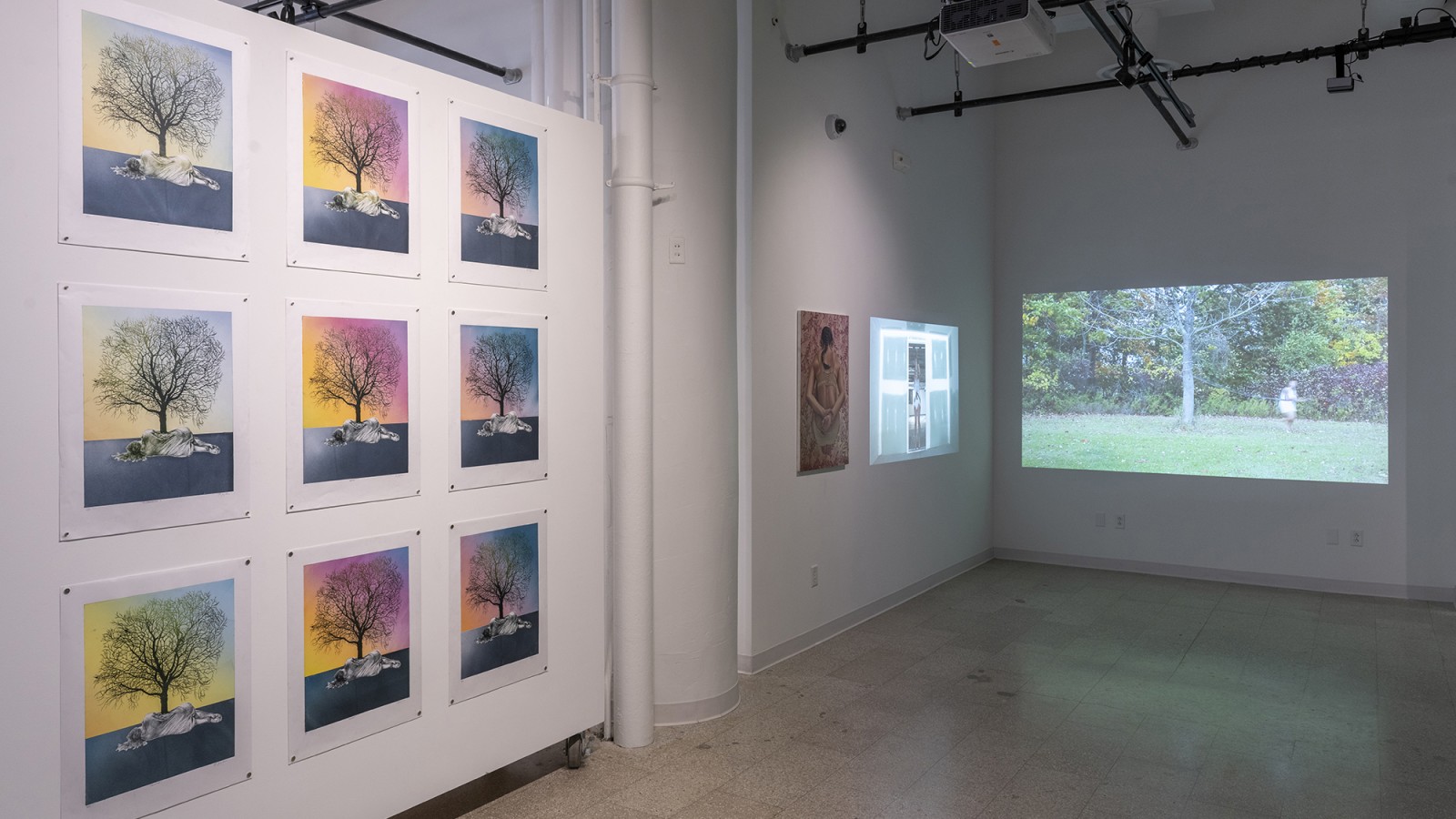 Paintings are mounted on one wall while a video plays on another.