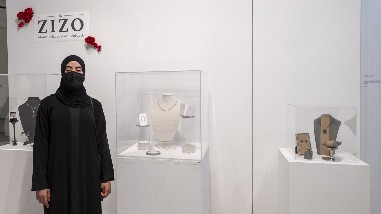 A student stands next to jewelry designs.