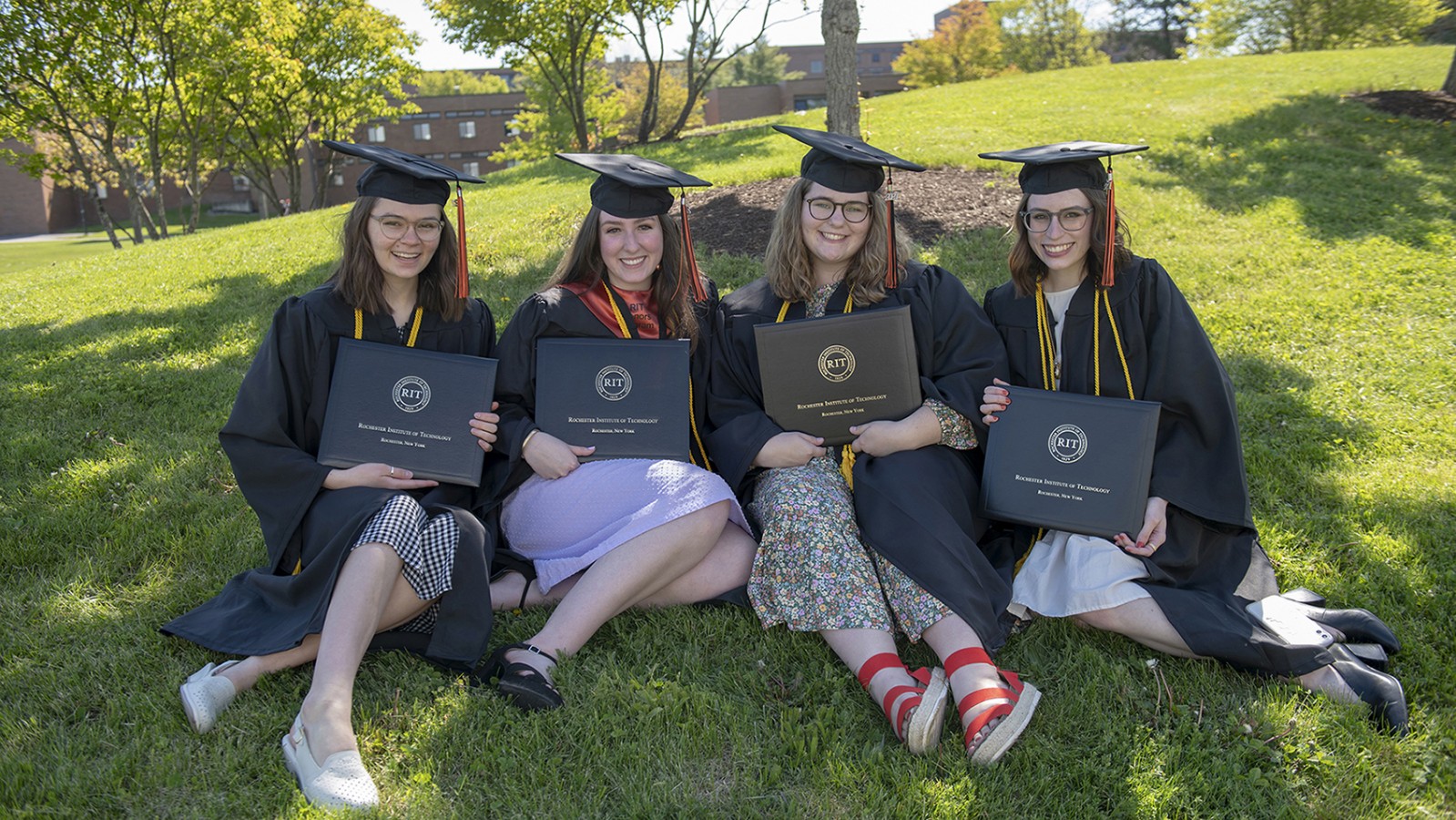 Four students pose for a photo holding their diplomas.