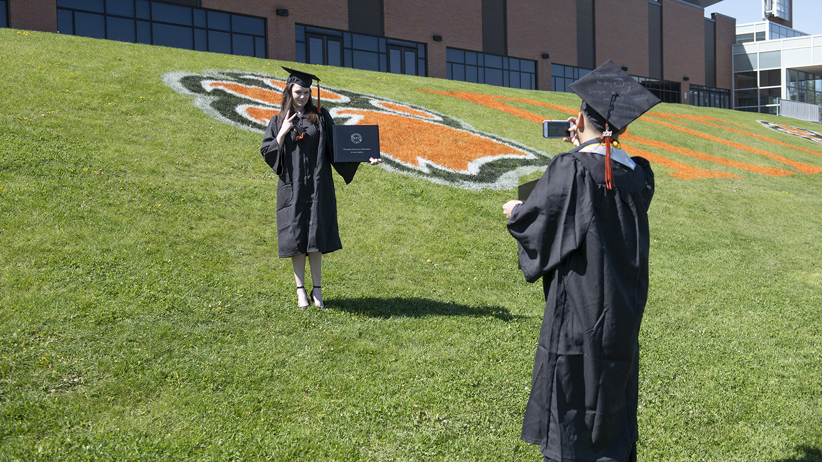 One students takes a photo of another on the lawn.