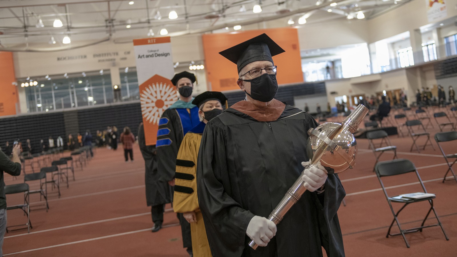 Mace bearer leads a line with Provost Ellen Granberg and Dean Todd Jokl.