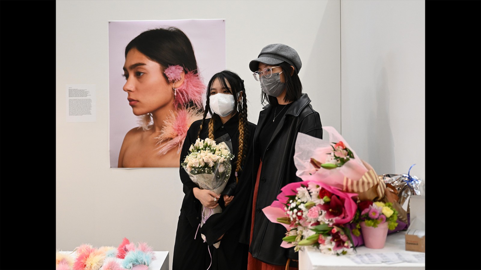Two artists stand in a gallery surrounded by artwork.
