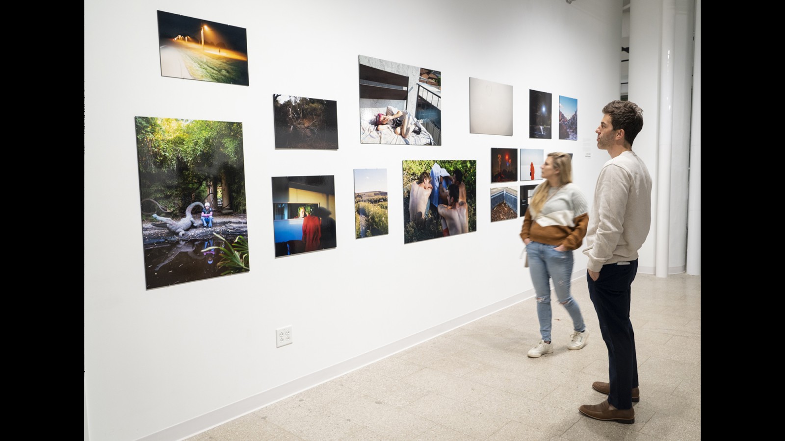 Gallery visitors look at photographs on a wall.