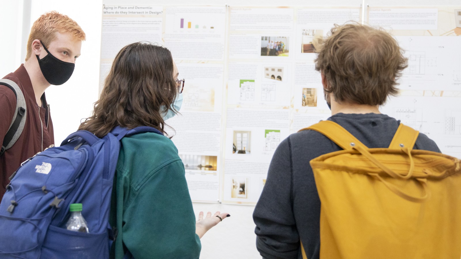 Three students look at posters on a gallery wall.