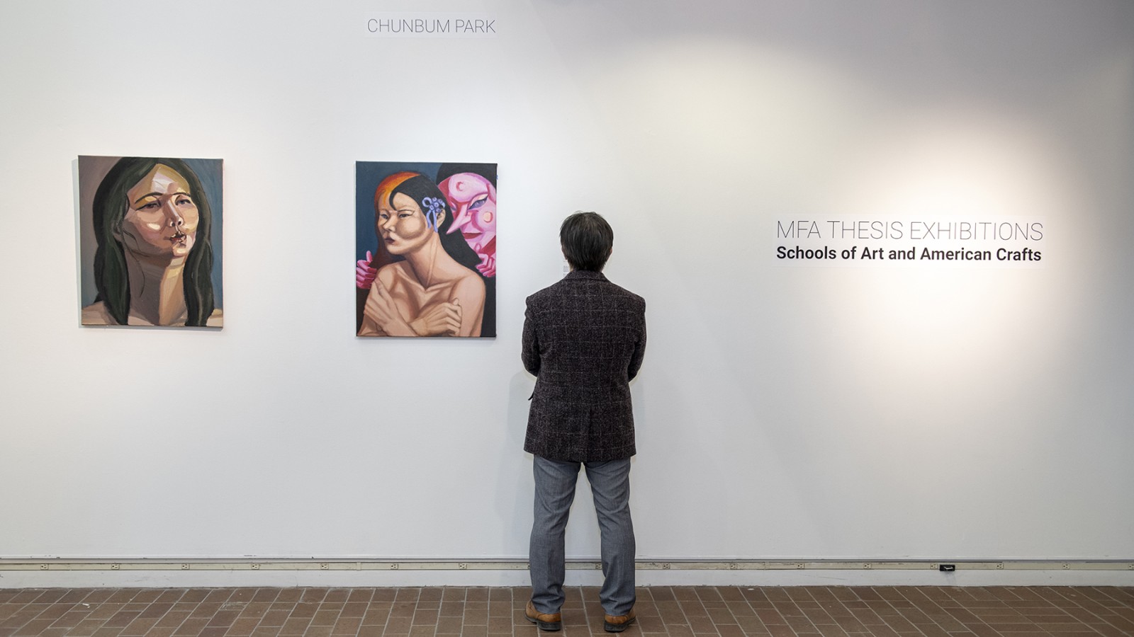 A gallery visitor looks at paintings on a wall.