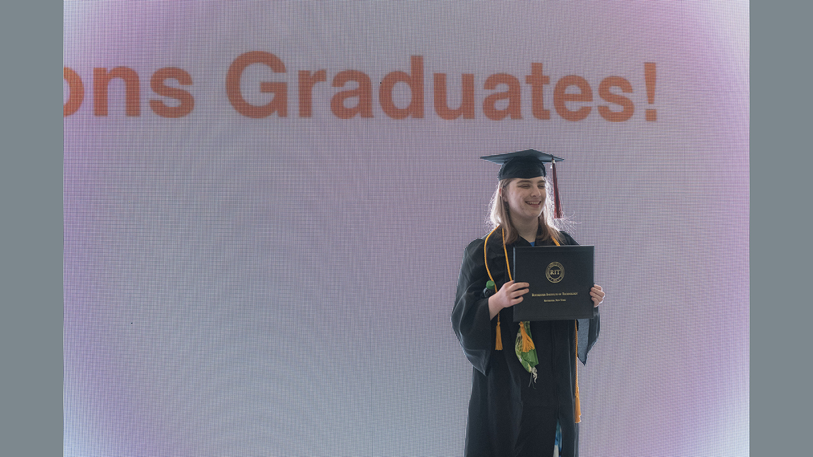 A new graduate poses for a photo in front of MAGIC's large LED wall.