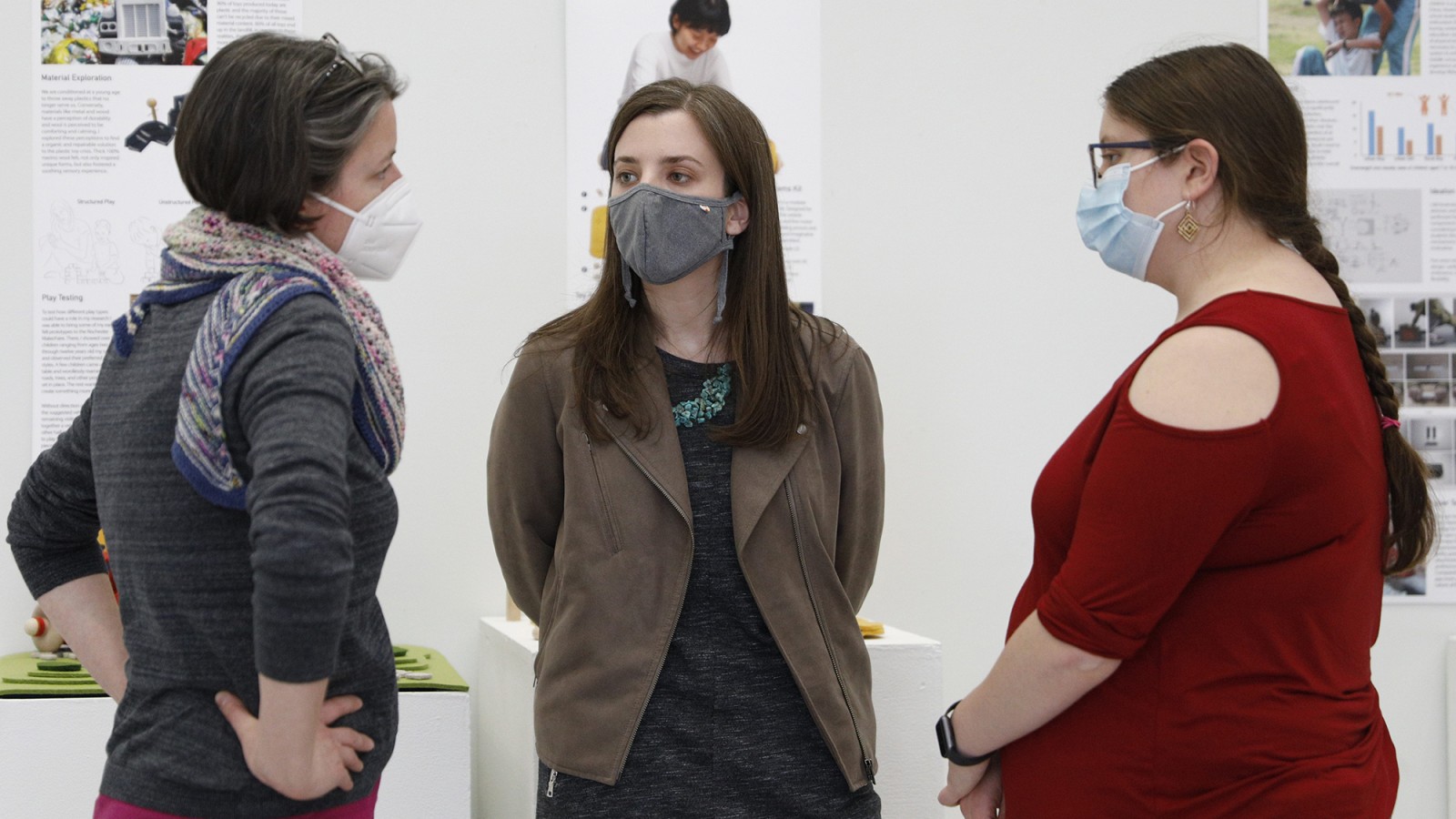 Three people talk in a gallery.