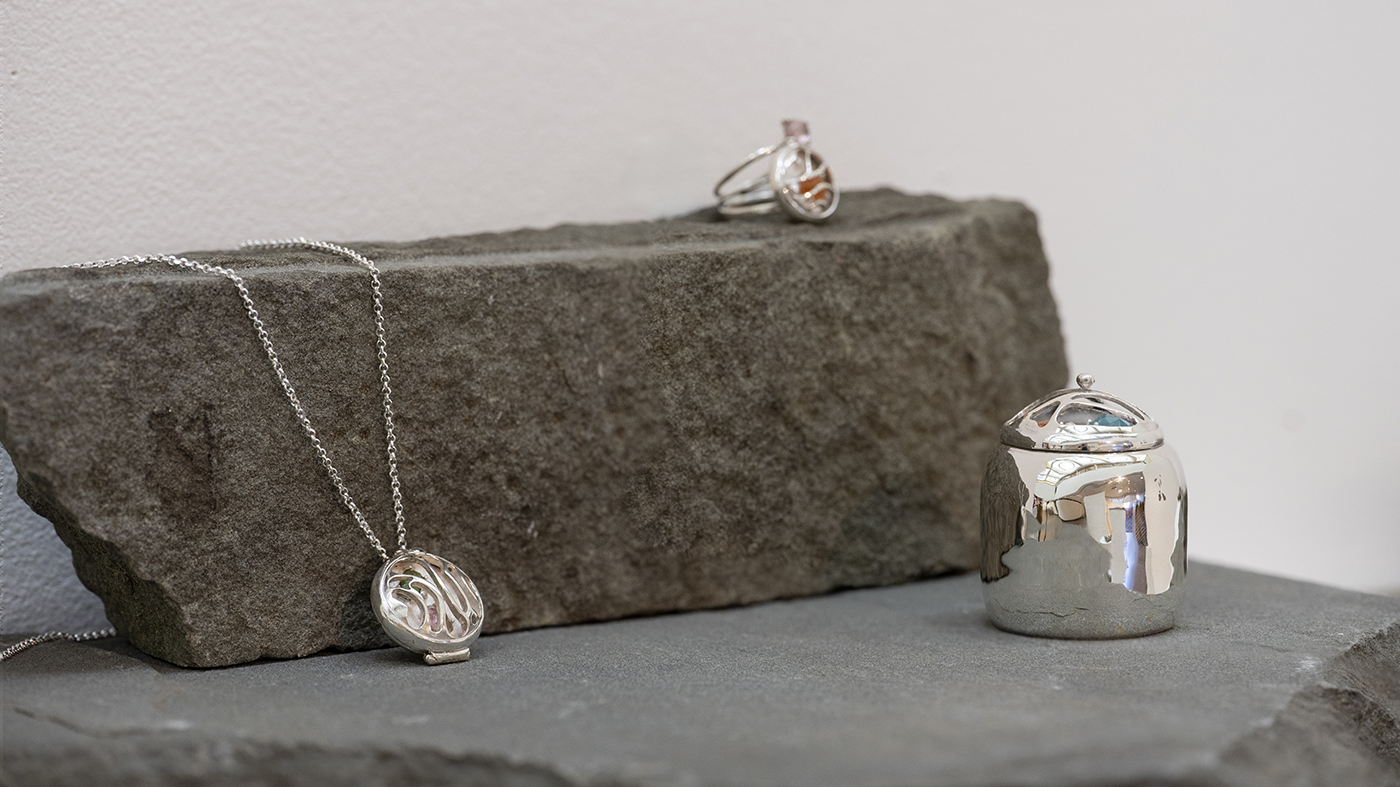 Silver jewelry is displayed on rocks.